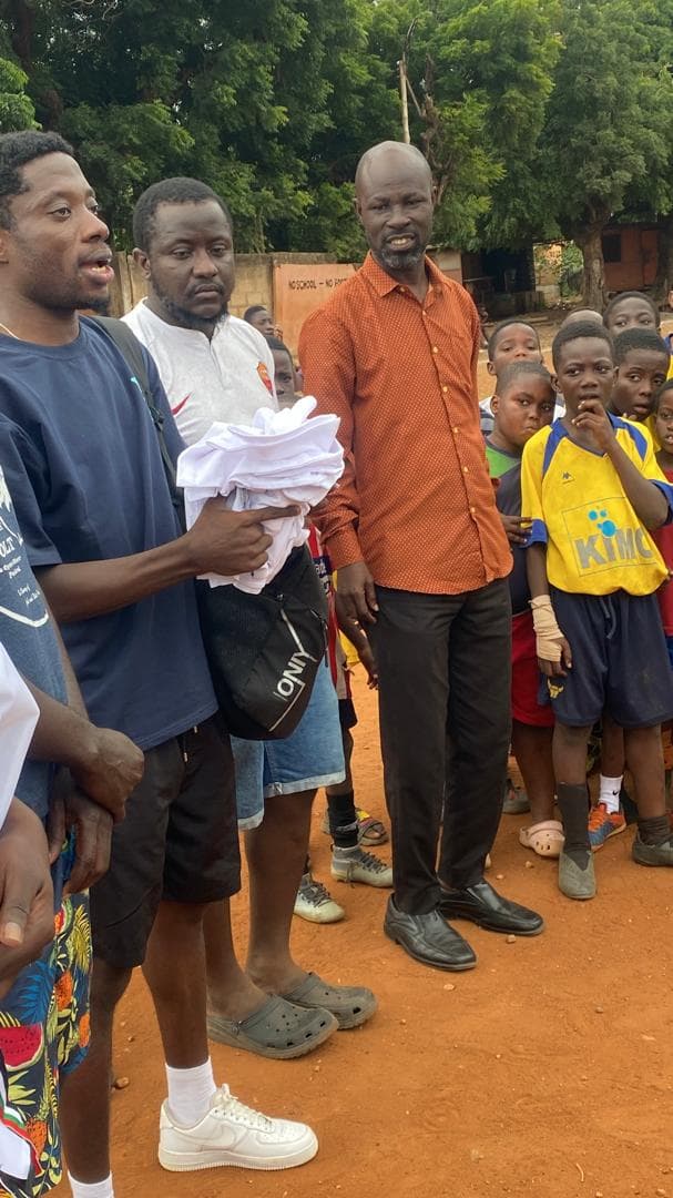 Organizers handing white kit bundles to young players on a dirt pitch