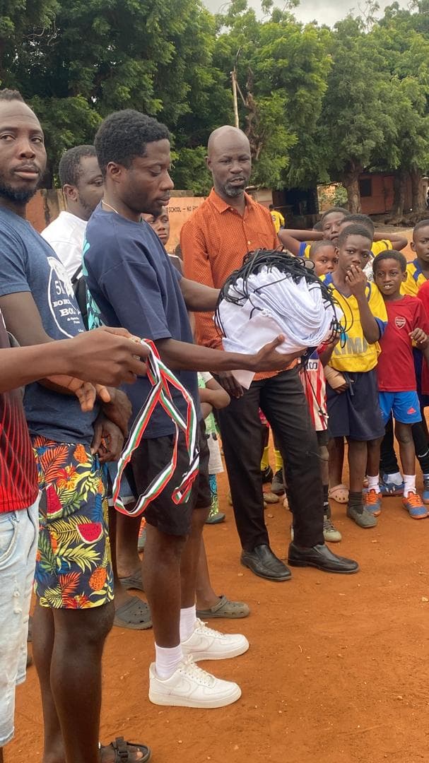 Coaches distributing red, white and green ribbon lanyards to players on the pitch