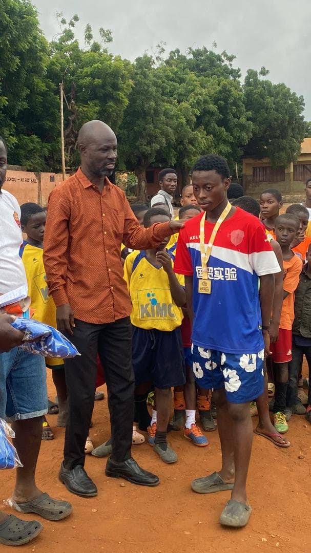 A coach places a hand on the shoulder of a boy wearing a gold medal on the pitch