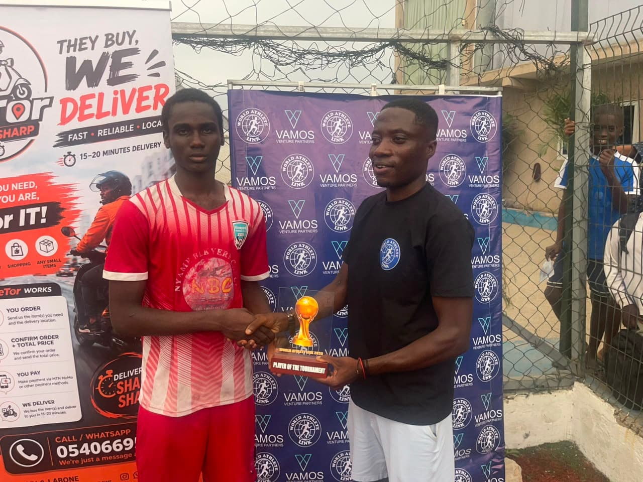 Two players shake hands while holding a Player of the Tournament trophy