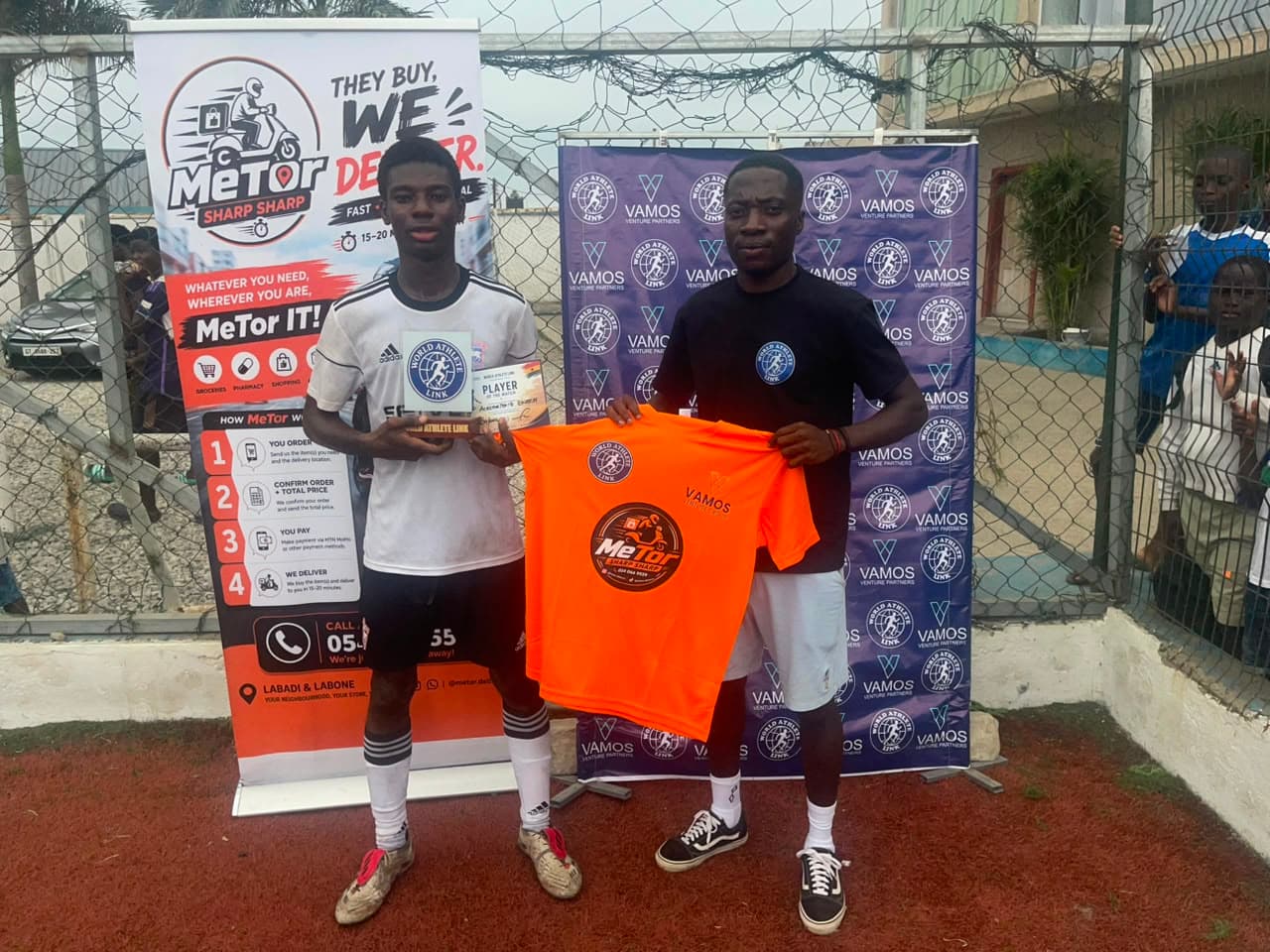 Two players pose with a trophy and an orange jersey in front of the WAL backdrop