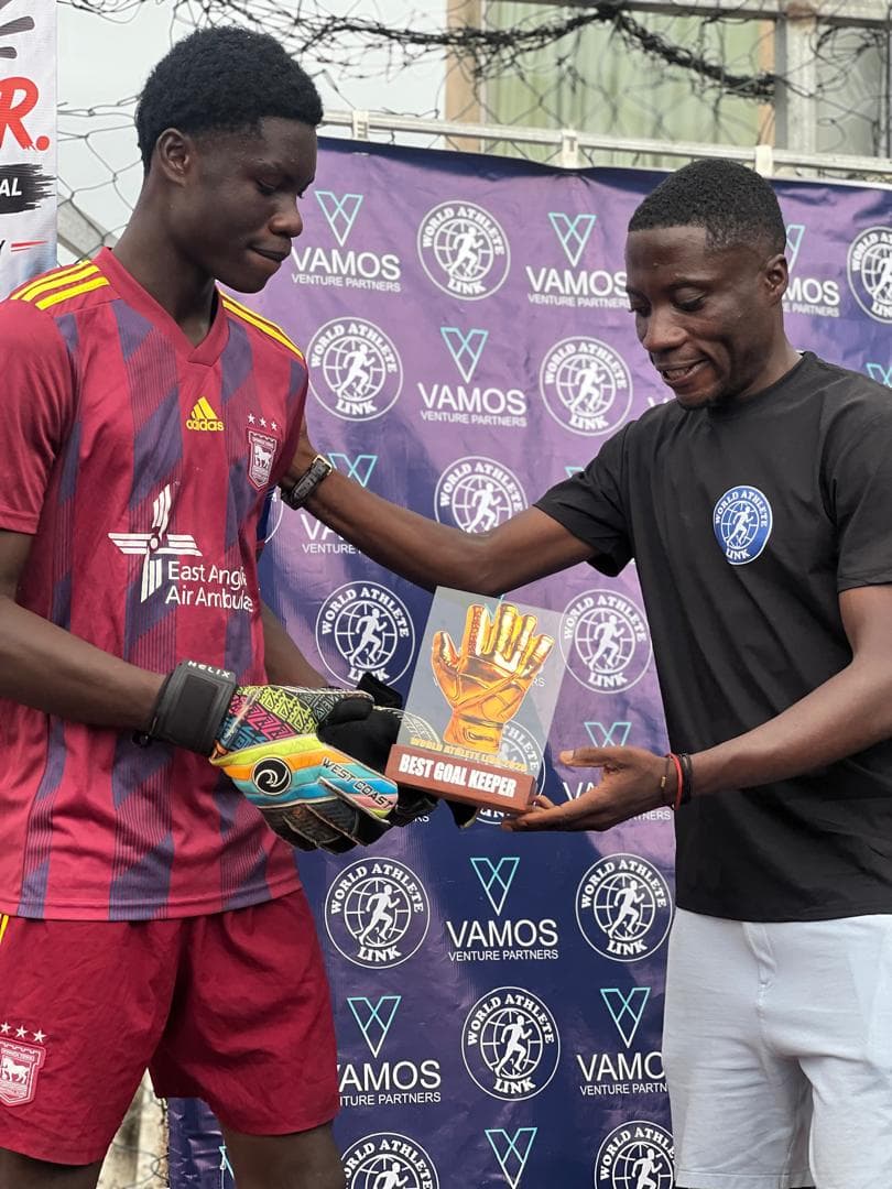 Two men exchange a Best Goal Keeper glove trophy in front of the WAL backdrop